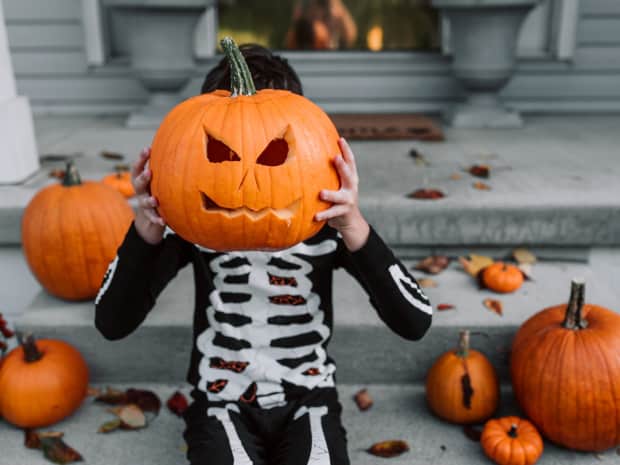a kid in a skeleton costume holding up a carved jack-o'-lantern to their face